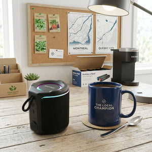 Sharp GX-BT190-BK compact black speaker on a wooden desk next to a coffee mug for size reference.