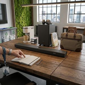 Sharp HT-SBW53121 soundbar and subwoofer on a wooden desk next to a coffee maker and briefcase.